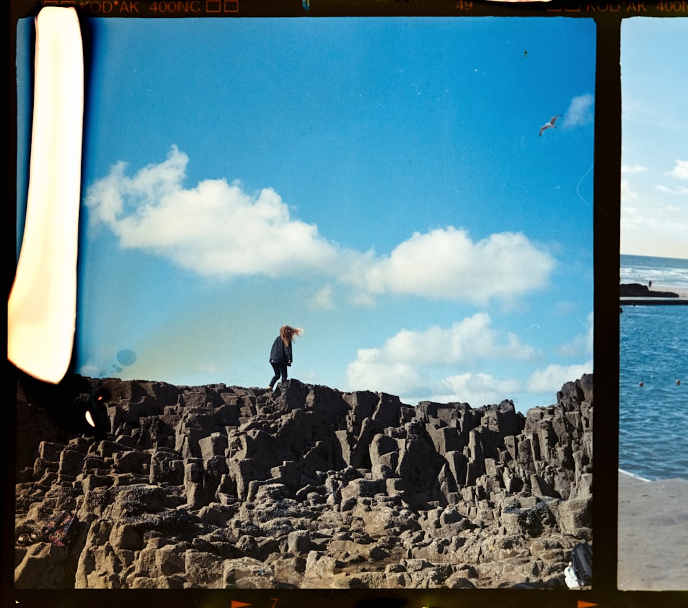 man in black jacket standing on rocky hill under blue sky during daytime