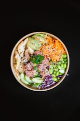 Colorful pokeball bowl with fresh fish, avocado, and bright toppings in a rustic wooden bowl.
