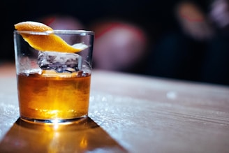 Close-up of a smoky, amber cocktail in a rugged glass with a charred orange twist.