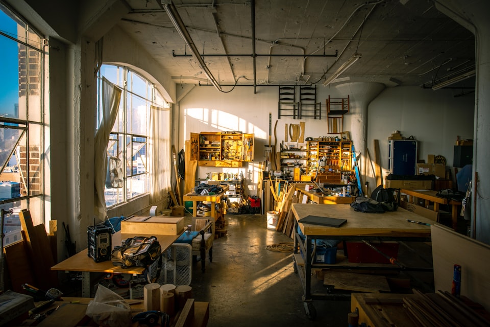 A workshop filled with materials and workspaces lit by sunlight coming in through the window