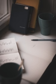 An open notebook with a pen resting on top, surrounded by books.