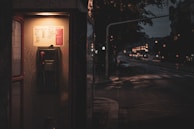 A nighttime street scene featuring an isolated phone booth glowing under a streetlamp.