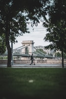 A rider cruising along a scenic riverside path on a red Tuya Smart electric scooter with greenery in the background.