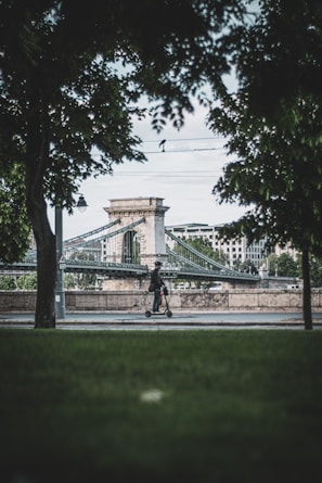 A rider cruising along a scenic riverside path on a red Tuya Smart electric scooter with greenery in the background.