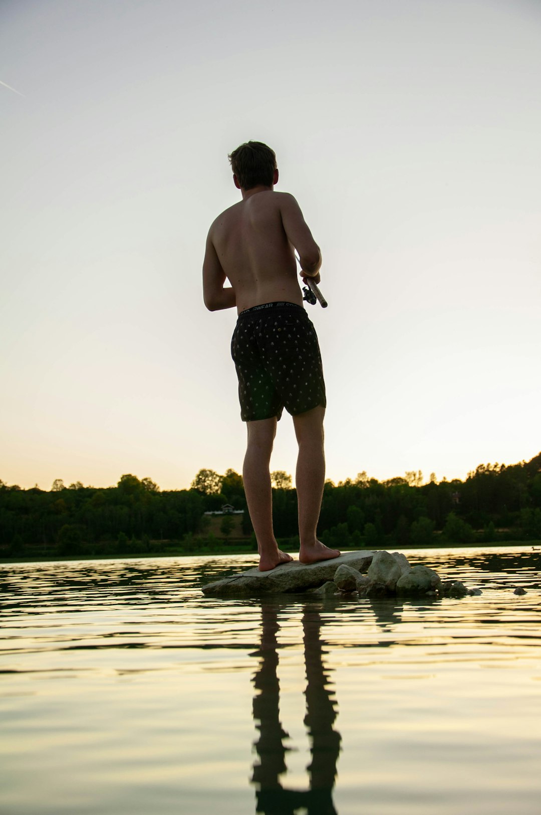 man in black and green floral shorts standing on body of water during daytime