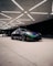 A sleek sports car with a vibrant chameleon paint finish is parked under a geometrically patterned ceiling with bright lighting. The car's dynamic design is complemented by custom black rims and low-profile tires. In the background, there is another vehicle, partially visible.