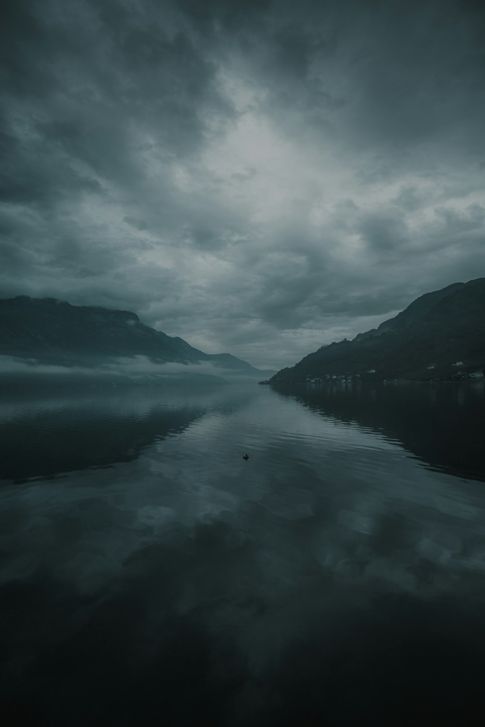 body of water near mountain under cloudy sky during daytime