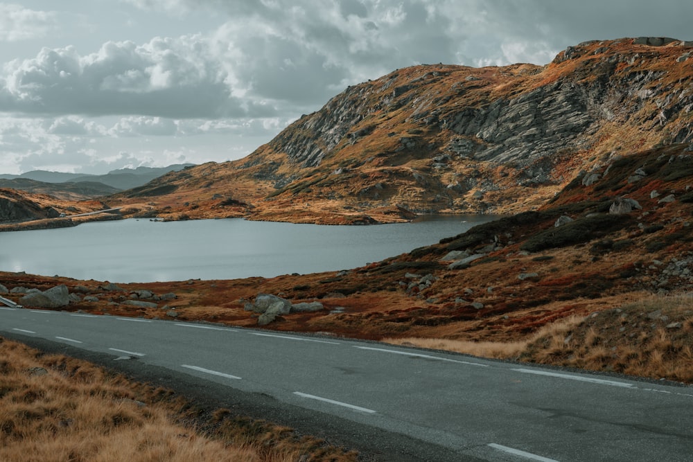 gray asphalt road near brown mountain under white clouds during daytime