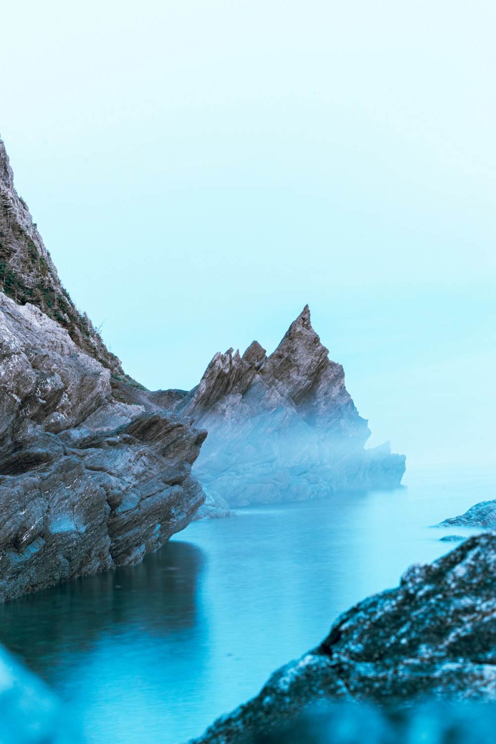 montanha rochosa marrom ao lado do mar azul sob o céu branco durante o dia