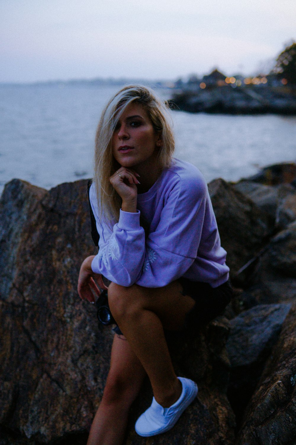 woman in purple long sleeve shirt sitting on rock near body of water during daytime