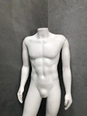 A headless white mannequin torso stands upright against a textured gray wall, displaying a muscular physique.
