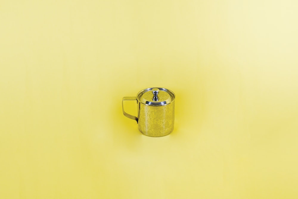 a yellow wall with a metal mug on it
