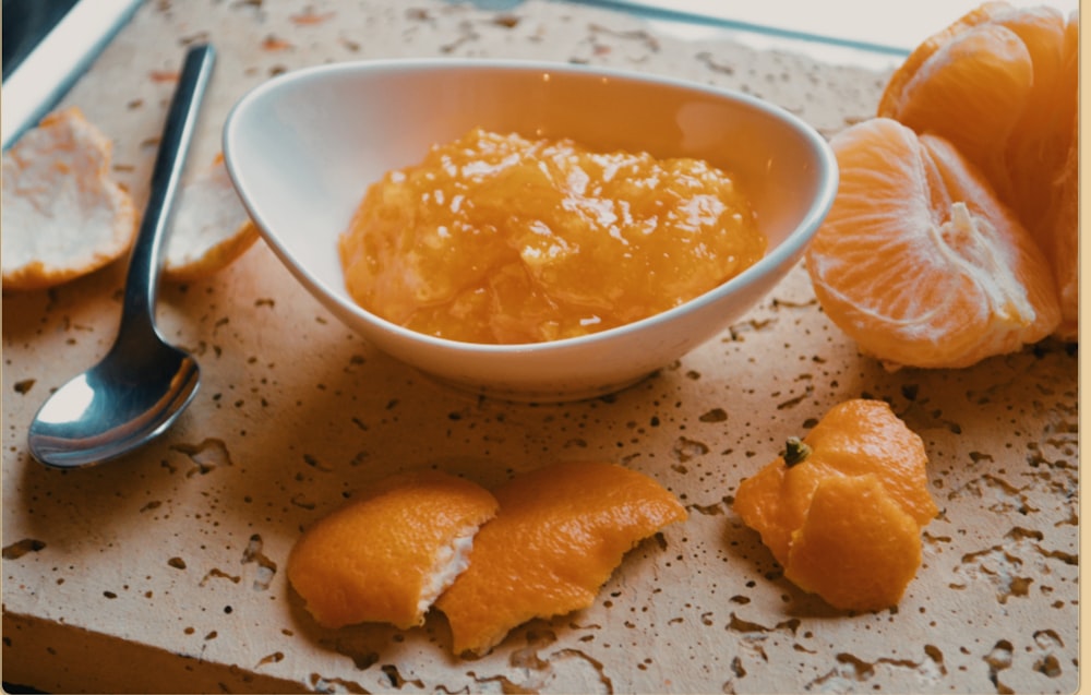 a white bowl filled with orange sauce next to sliced oranges