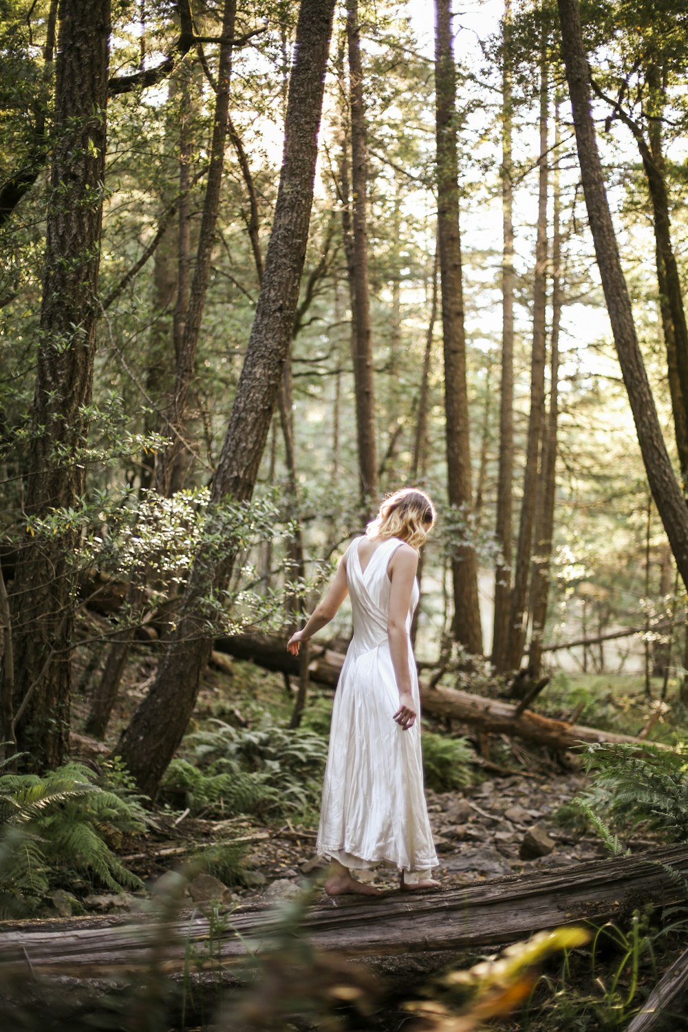 昼間の森に立つ白いドレスの女性