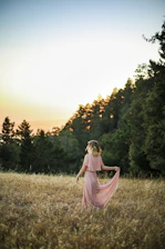 A cheerful woman wearing a flowing pink dress against a soft sunset.