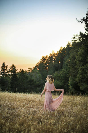 A cheerful woman wearing a flowing pink dress against a soft sunset.