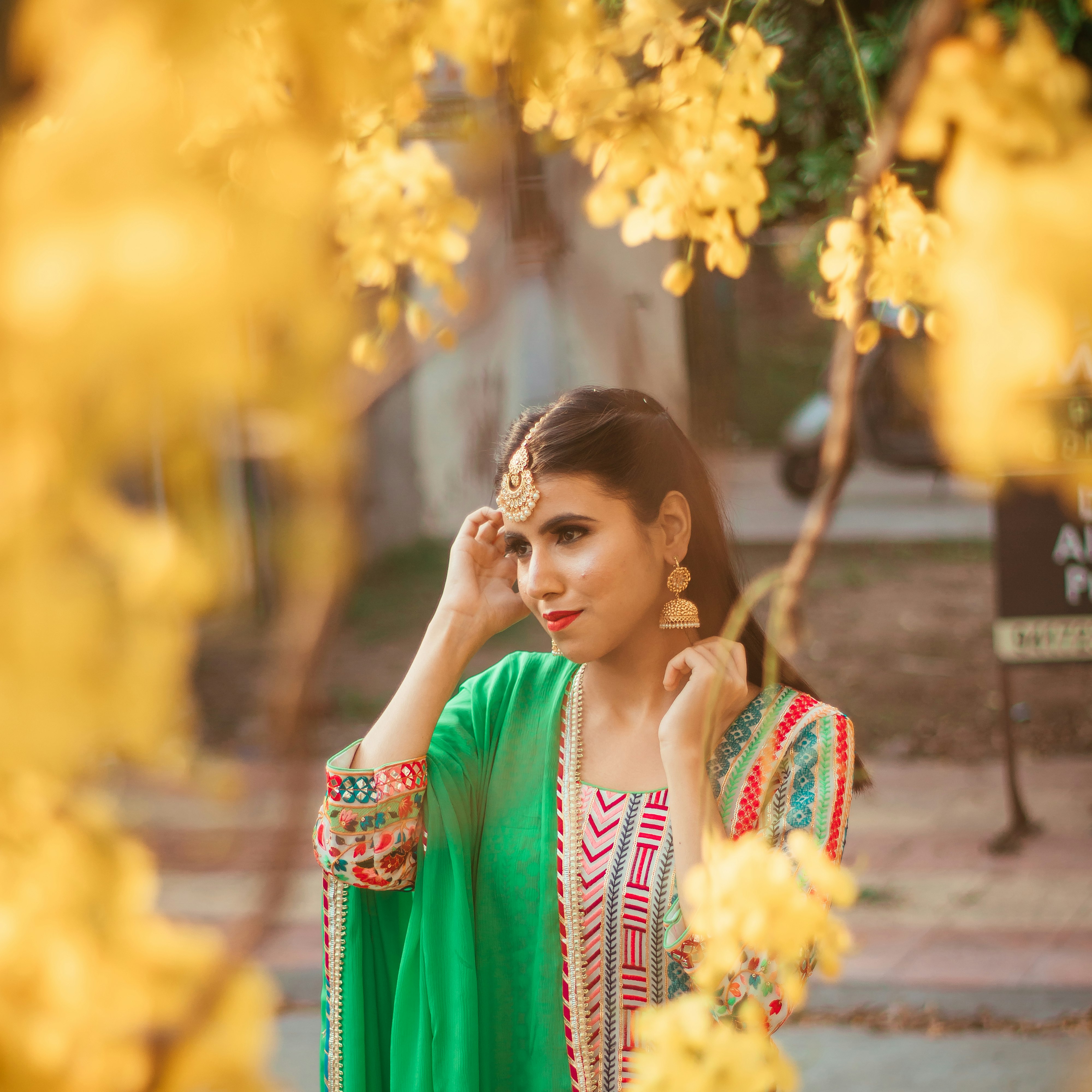 woman in red and white sari standing near yellow flowers during daytime