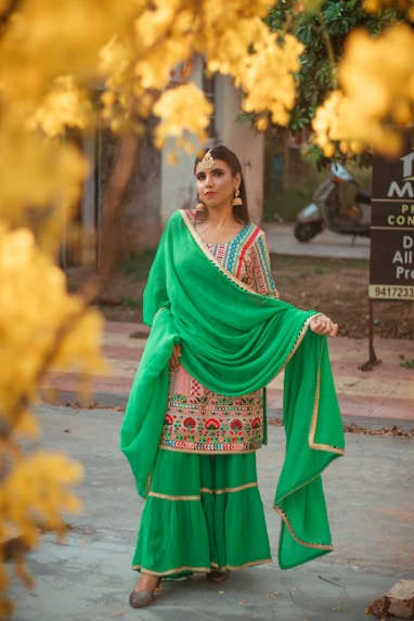 woman in green and red sari standing on gray asphalt road during daytime