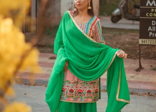 woman in green and red sari standing on gray asphalt road during daytime