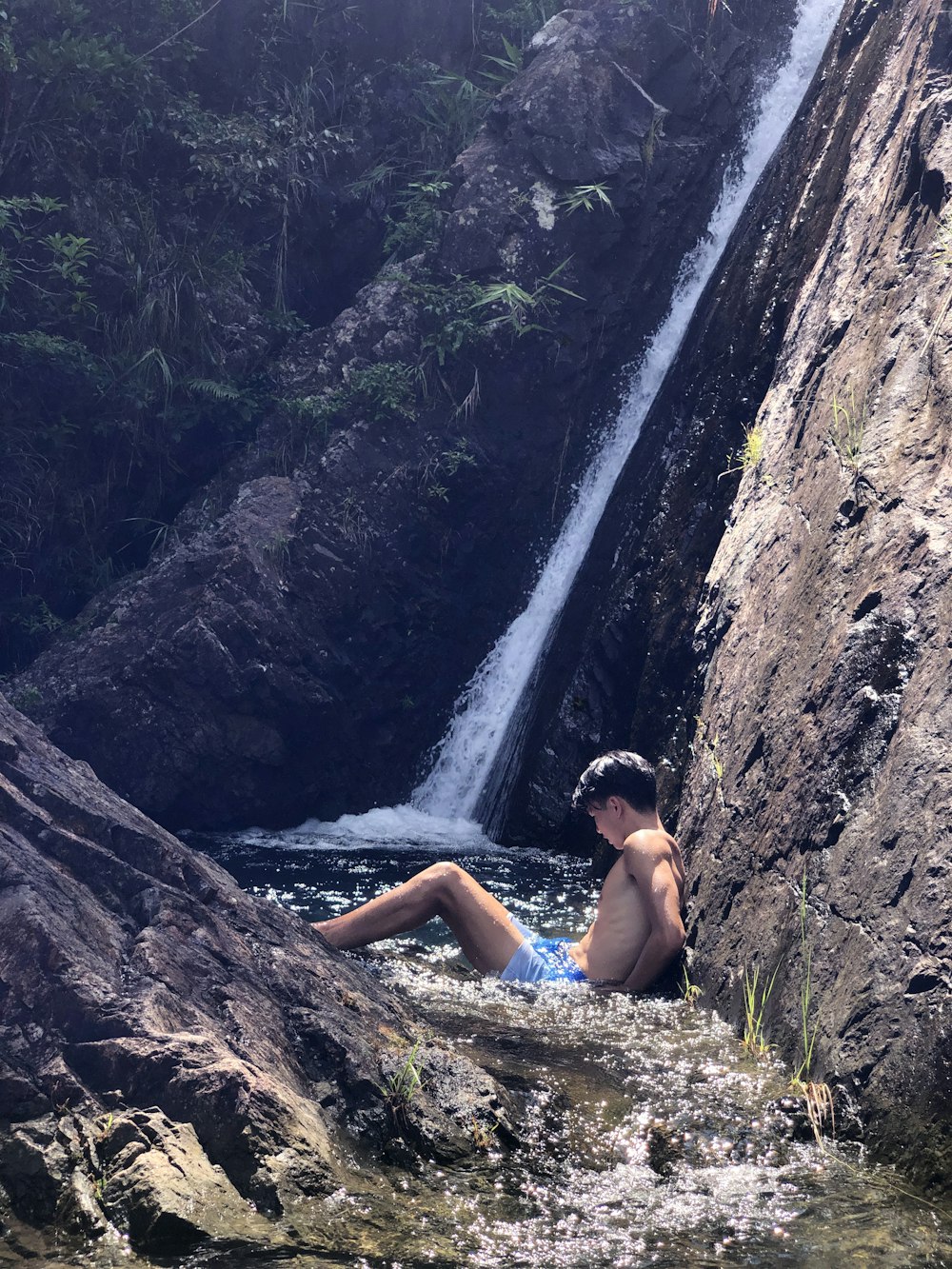 woman in blue bikini sitting on rock near waterfalls during daytime
