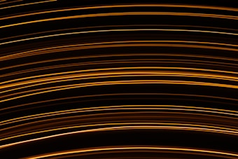 Curved, parallel lines of warm golden light create an abstract pattern against a dark background, suggesting motion and energy.