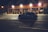 A blue car is driving on a dimly lit street at night. The scene is in front of a building with illuminated signage, indicating a business called North Atlantic Supplies Inc.