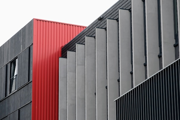 A modern architectural facade composed of geometric panels, primarily featuring a combination of red, gray, and black colors. The design features vertical lines and a mix of textures.