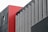 A modern architectural facade composed of geometric panels, primarily featuring a combination of red, gray, and black colors. The design features vertical lines and a mix of textures.