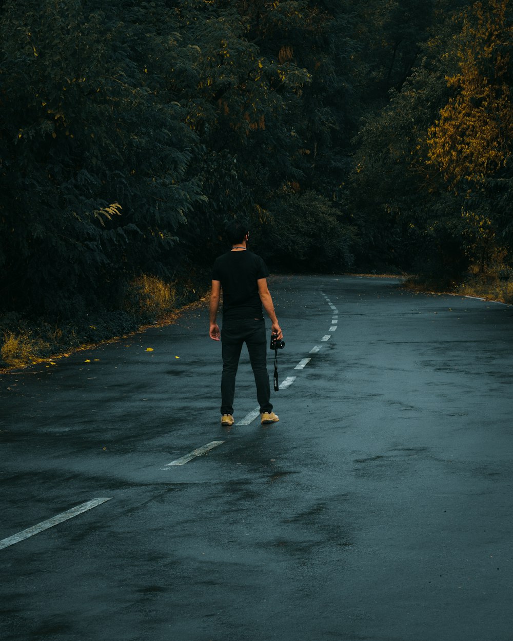 Hombre con chaqueta negra y jeans de mezclilla azules caminando por una carretera de asfalto gris durante el día