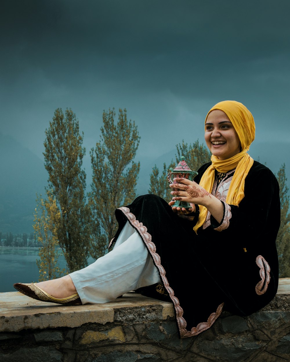 woman in black jacket and white hijab sitting on brown wooden log during daytime