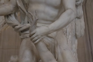 A detailed close-up view of a marble sculpture depicting a dynamic and intricate scene featuring human figures. The focus is on the interlocking hands and muscular arms, emphasizing the tension and movement captured in the stone.