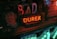 A dimly lit scene depicting a vintage and eclectic collection of objects, including a large red neon sign reading 'Durex'. To the left, there is a mannequin head of a man wearing a cap, and several other items including a canister, letters forming part of a word, and a small vintage toy bus.
