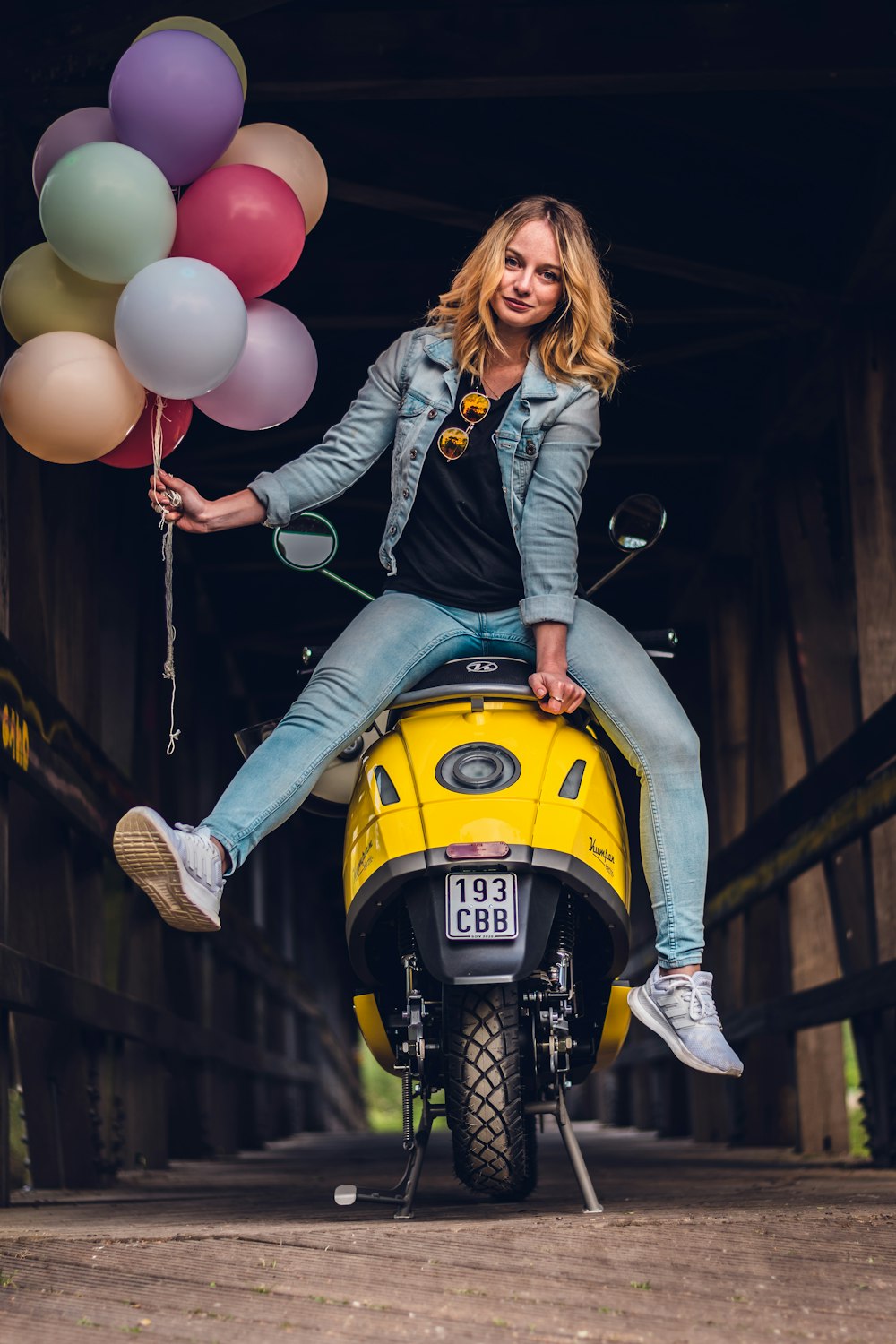 woman in black leather jacket and blue denim jeans riding yellow motorcycle holding balloons