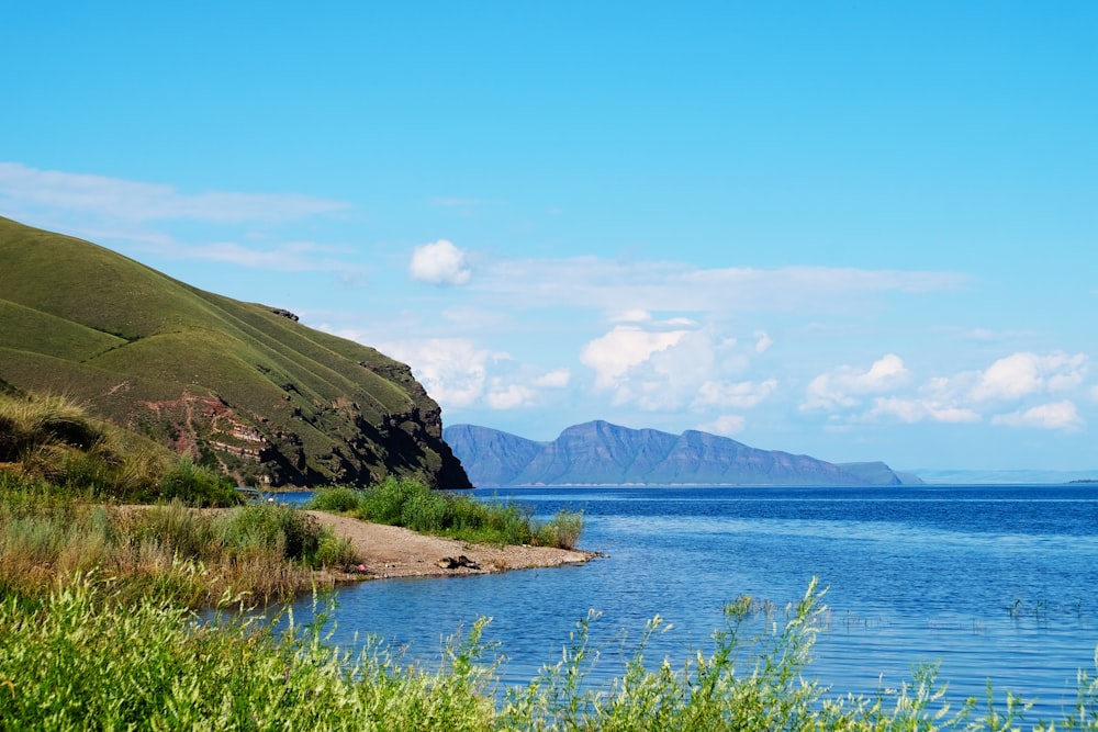 green grass field near body of water and mountain during daytime