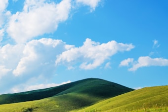 A serene landscape featuring gentle green hills under a vibrant blue sky scattered with fluffy white clouds.