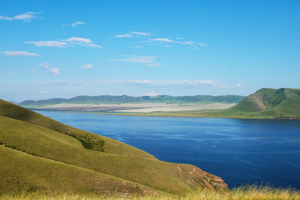 green grass field near body of water under blue sky during daytime