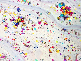 A swirling background with a mix of scattered, colorful particles and circular objects. The particles vary in size and are primarily in shades of blue, yellow, pink, and red, creating a vibrant and dynamic pattern.