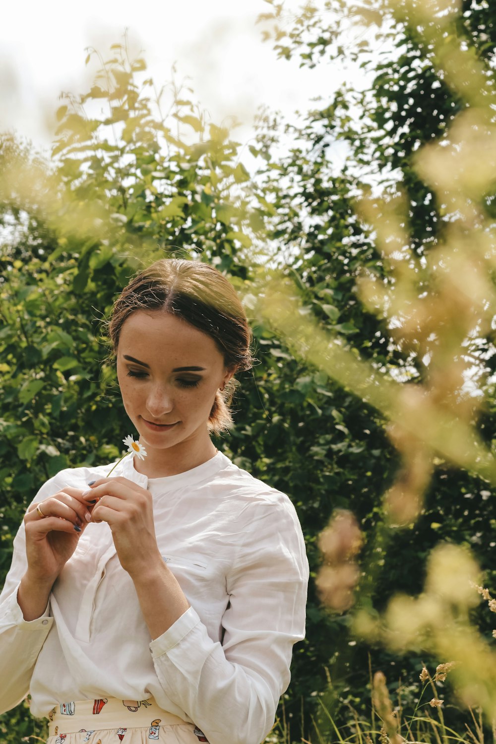 woman in white crew neck t-shirt holding white flower during daytime