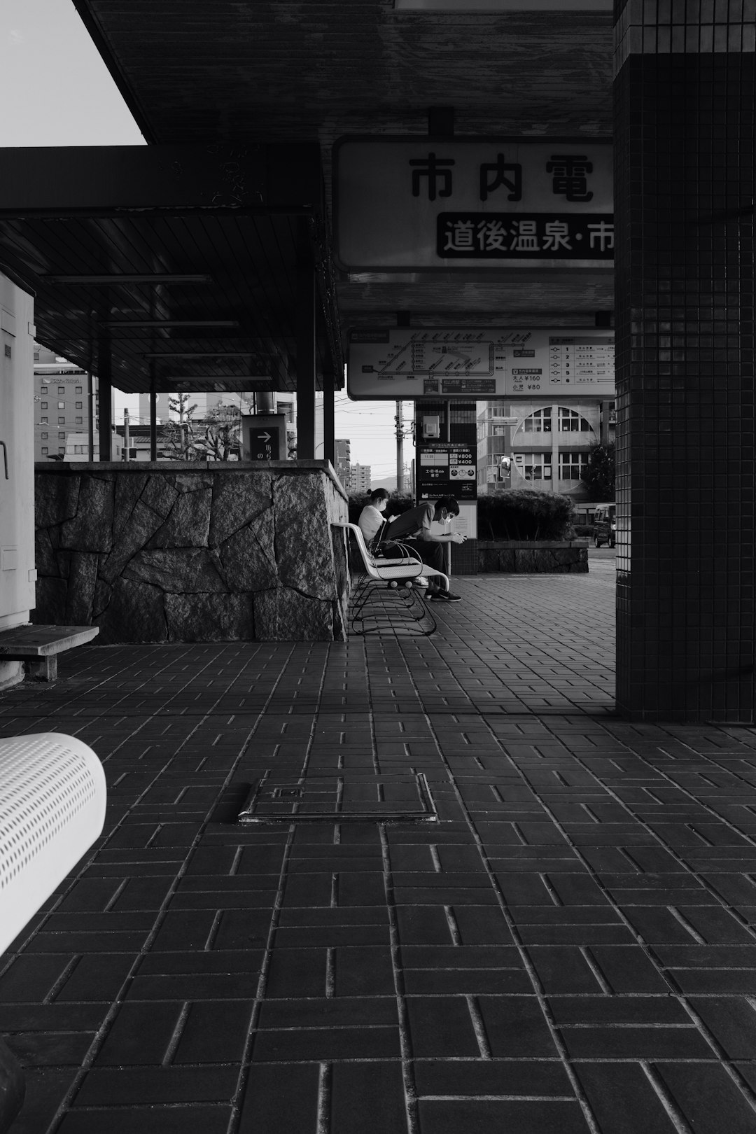 grayscale photo of woman sitting on chair near store