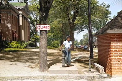 a young african american boy drinks out of a fountain labeled 'colored' colorized zoom background