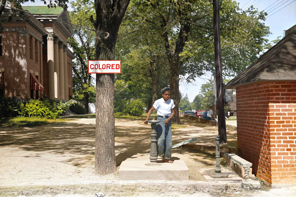 A young African American boy drinks out of a fountain labeled 'Colored'