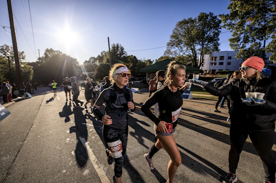 A diverse group of runners smiling and crossing a finish line together at a sunny community race.