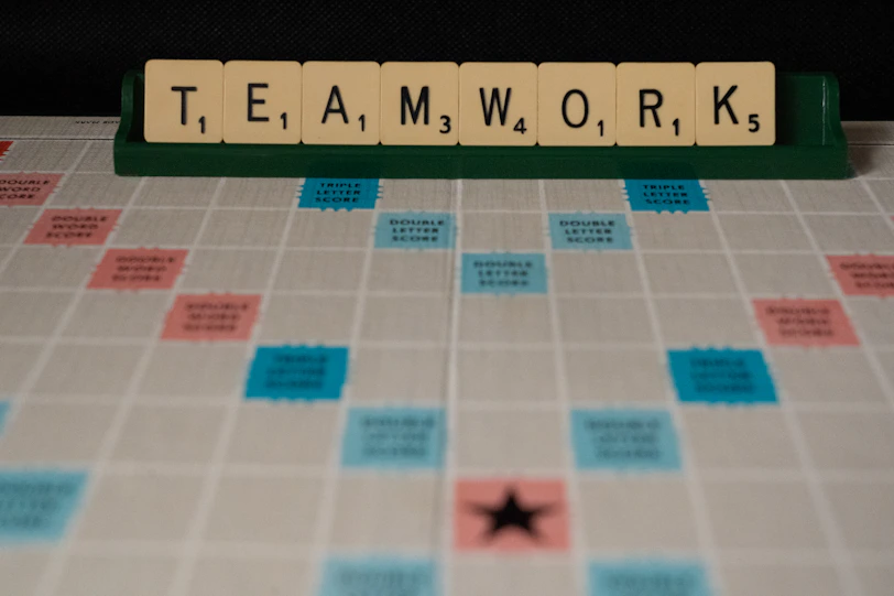 Scrabble tiles spelling teamwork on a green rack above a game board