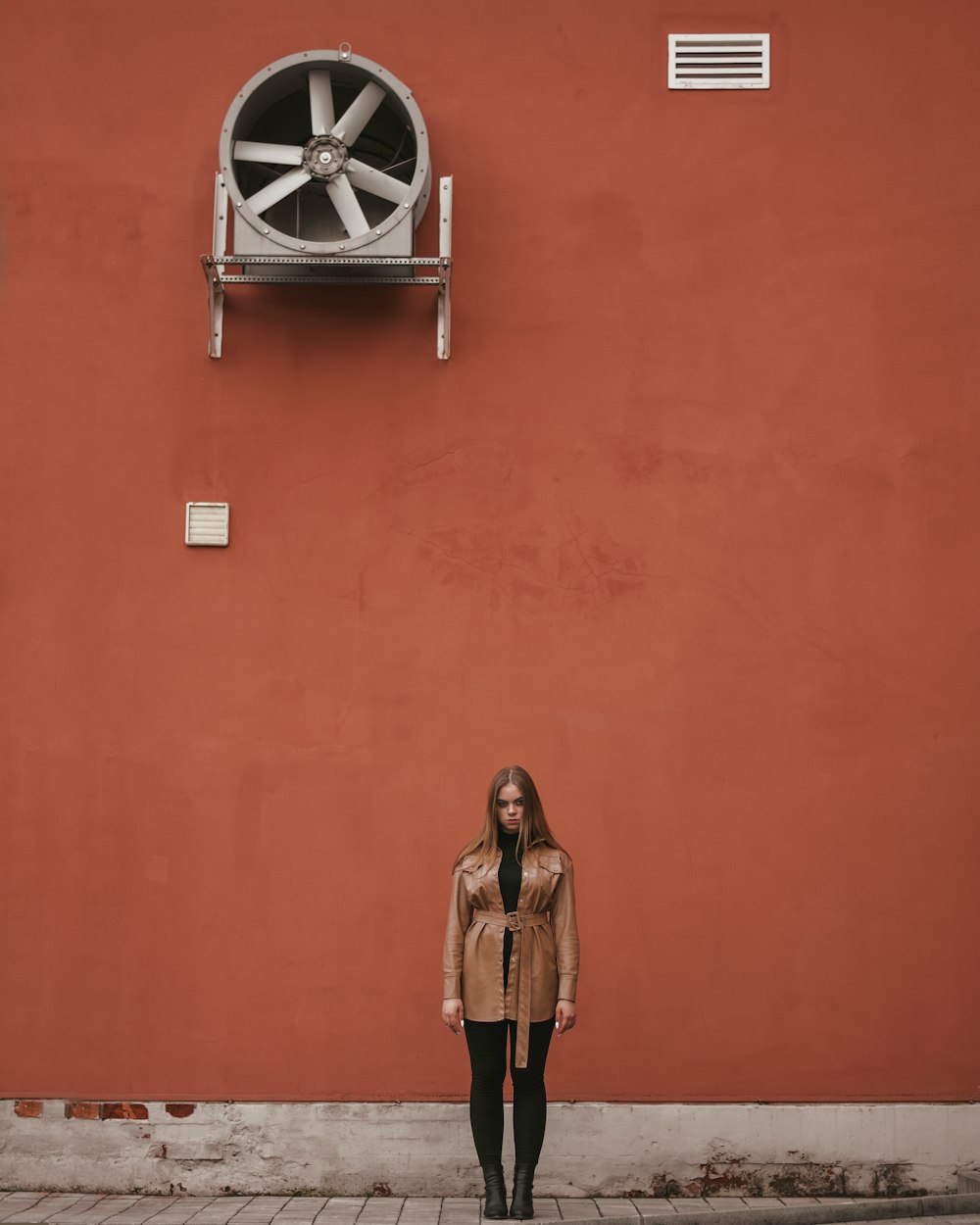woman in brown coat standing beside orange wall