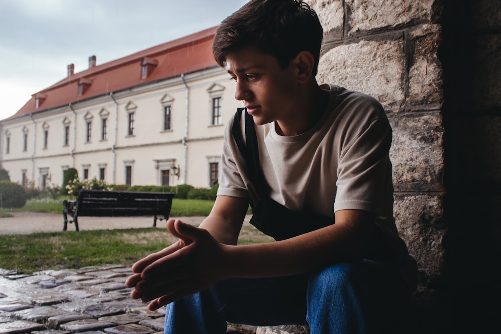 man in gray crew neck t-shirt and blue denim jeans sitting on gray concrete bench