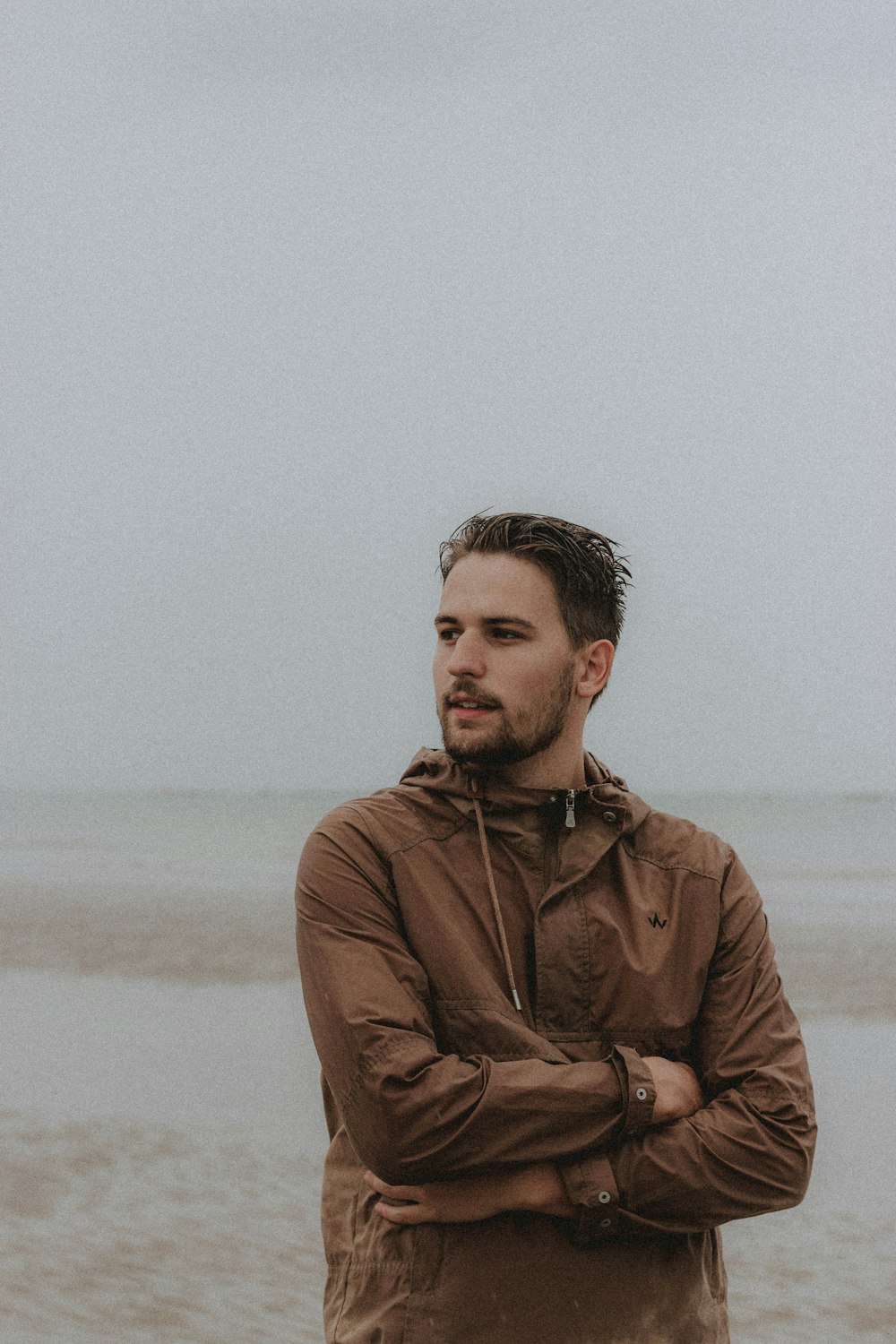 낮 동안 해변에 서 있는 갈색 재킷을 입은 남자