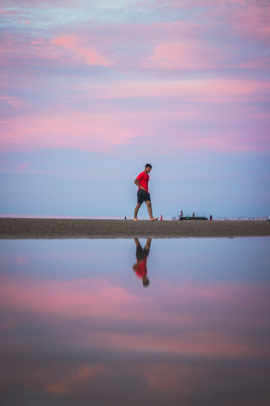 man in black shirt and black shorts walking on beach during daytime