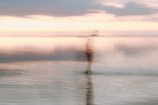 Blurred silhouette of a lone figure disappearing into fog over a lake at dawn.