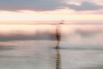 Blurred silhouette of a lone figure disappearing into fog over a lake at dawn.