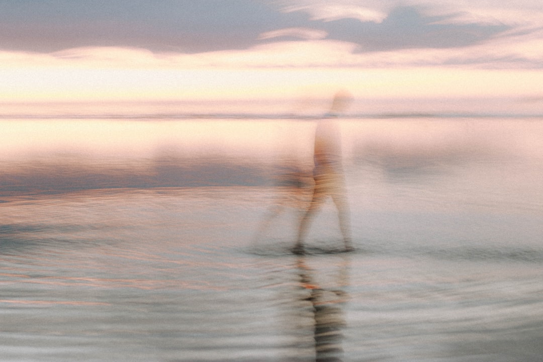 person in white shirt and black pants standing on sea shore during daytime